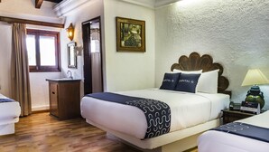 Hotellihuone, jossa on sänky, yöpöytä, lamppu ja taulu seinällä.