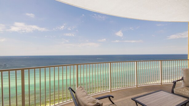 A balcony with a view of the ocean, a chair, and a table.