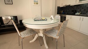 Una cocina moderna con armarios blancos, un salpicadero de azulejos negros y una mesa redonda de cristal con dos sillas de estructura metálica.