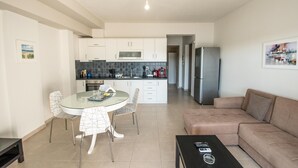 Una cocina moderna con armarios blancos, un microondas y un refrigerador de acero inoxidable. Hay un comedor con sillas y un sofá en la sala.