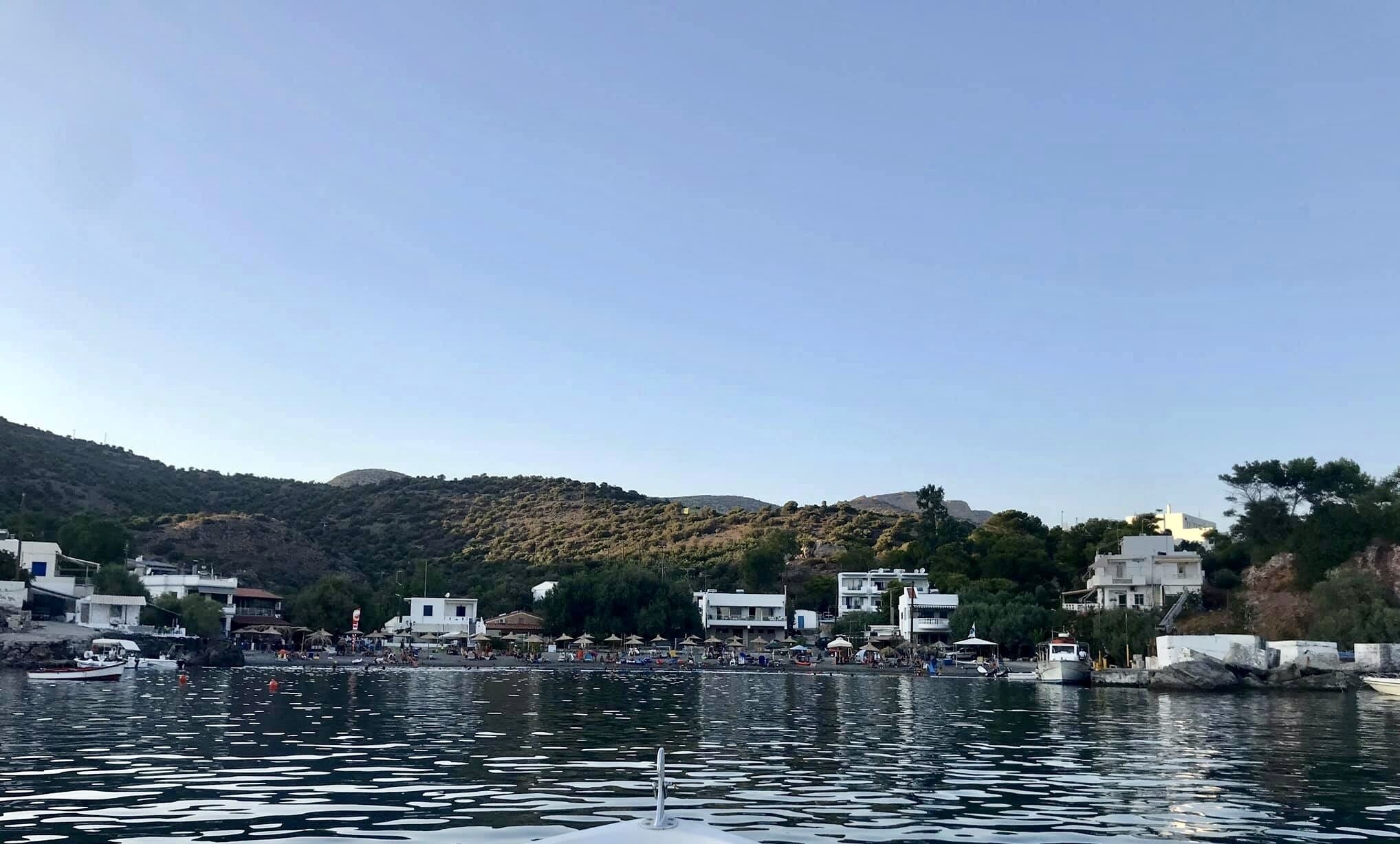 Una cittadina costiera con edifici lungo il lungomare, cielo sereno e barche in acqua.