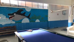 Une table de billard dans une pièce dont un mur est décoré d’une fresque représentant un requin, et où l’on trouve également un panier de basket.
