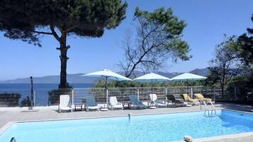 A swimming pool with lounge chairs and umbrellas, surrounded by trees and a view of the sea.