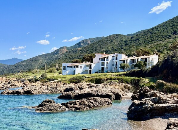 A coastal property with a white building featuring multiple balconies, situated on a rocky shoreline with clear blue water. - Apartment by the sea for 4 (CALCATOGGIO)