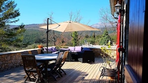 An outdoor deck with a table and chairs, a large umbrella, and a stone wall.