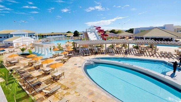A resort pool area with multiple pools, lounge chairs, umbrellas, and a water slide.