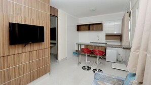 A compact kitchen with a flat-screen TV, wooden paneling, a small bar area with red stools, and a white refrigerator.