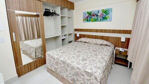 A bedroom with a bed, a wardrobe, a mirror, a painting, and a telephone.