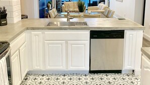 A modern kitchen with white cabinetry, a central island with a dishwasher, and a patterned tile floor.