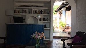 A living area with a blue cabinet, a television, and a vase of flowers. There is a wooden chair with a purple cushion and a view of an outdoor patio with plants and a railing. - Casa LOBE (Ocosingo)