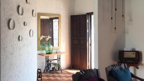 A room with a checkered floor, a wooden ceiling, a wall with circular decorations, a wooden door, and a table with a vase. - Casa LOBE (Ocosingo)