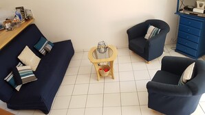 Een woonkamer met een donkerblauwe bank, twee fauteuils, een klein houten bijzettafeltje en een blauwe kast met lades.