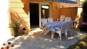 Een terras met een tafel, stoelen, een bloempot en een schuifdeur.
