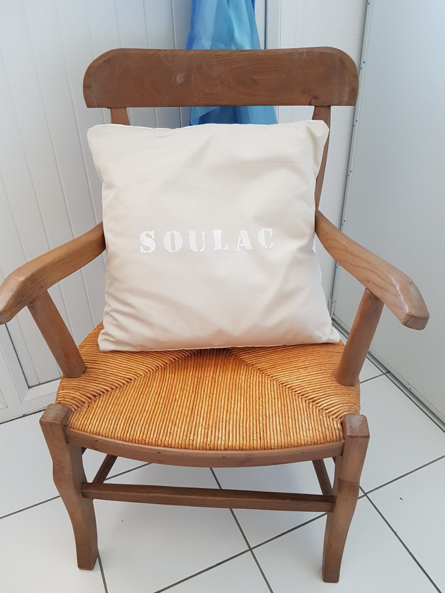 A wooden chair with a woven seat and backrest, and a cushion with the word "SOULAC" on it.