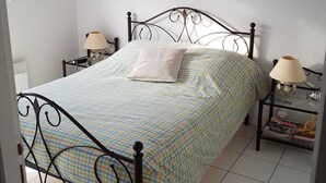 Een net opgemaakt bed met een geruit sprei, twee nachtkastjes met lampen, en een wandklok.