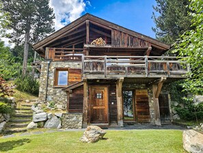 A rustic mountain cabin with a stone facade, wooden balcony, and a stone staircase leading to the entrance.
