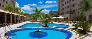 A swimming pool with palm trees and lounge chairs, surrounded by a building with balconies.