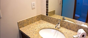 A bathroom with a granite countertop, a sink, a mirror, and a toilet visible through a glass partition.