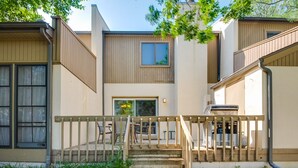 Ein modernes, zweistöckiges Haus mit einer Holzterrasse, einer Treppe und einer kleinen Grillgegend im Freien.