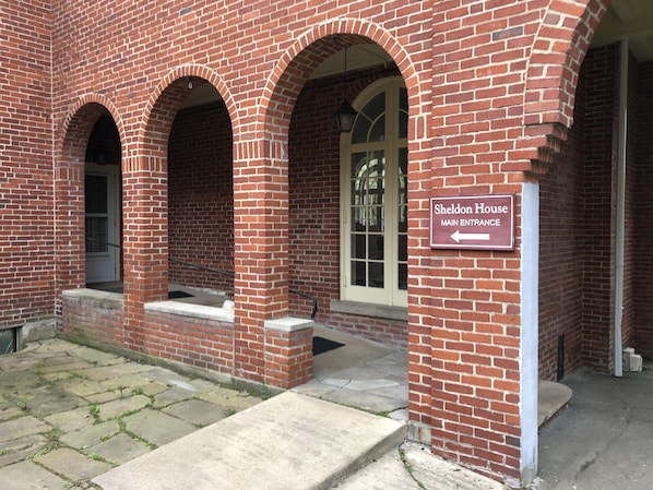 A brick building with arched doorways and a sign indicating the main entrance to Sheldon House.