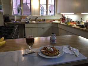A kitchen with a stove, a sink, and a window with a view of a brick building. There is a plate with waffles and a glass of iced coffee on the counter.