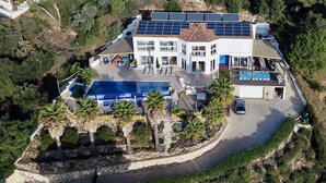 Vue aérienne d’une villa moderne dotée d’une piscine, de panneaux solaires et d’un mur de soutènement en pierre.