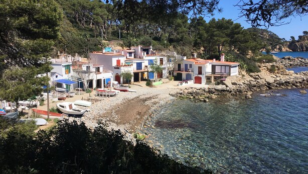 Un village côtier avec des bâtiments situés près de l’eau, des bateaux amarrés sur la plage et un paysage rocheux.