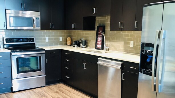 A modern kitchen with dark cabinetry, stainless steel appliances, and a tiled backsplash. - The Ultimate Vacation Spot! Modern at the same time! (Houston)