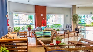 A lobby with wooden furniture, a red pillar, and large windows. - Riviera Park Thermas - Oferta Caldas (Caldas Novas)