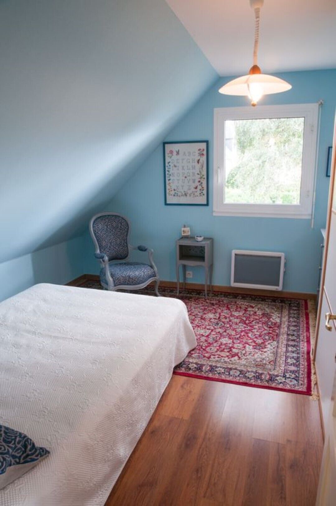 A bedroom with a bed, a chair, a radiator, a window, and a ceiling fan.