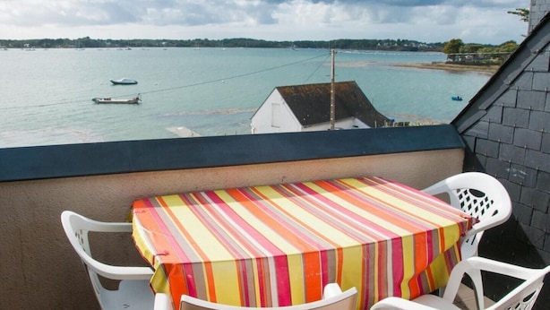 Een balkon met een tafel en stoelen, met uitzicht op een waterpartij met boten en een strand.
