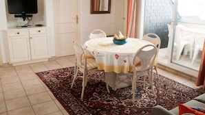 Een eetgedeelte met een ronde tafel, stoelen, een televisie en uitzicht op buiten.