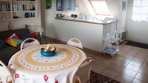Een gezellige woonkamer met een eettafel, een boekenkast en een keukenhoek met een raam.