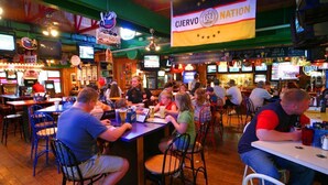 A crowded indoor venue with tables and chairs, featuring a prominent flag and various signs. - Cedar Stables Inn and Suites (Sandusky)