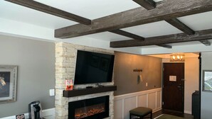 A modern room with a stone fireplace, a flat-screen TV, and a bench. - Cedar Stables Inn and Suites (Sandusky)