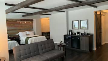 Een hotelkamer met twee bedden, een bank, een kitchenette en een groot raam.