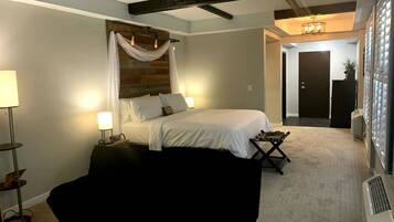 Quarto com cama, luminárias de cabeceira, mesa de cabeceira, uma cadeira preta e cabeceira de madeira.