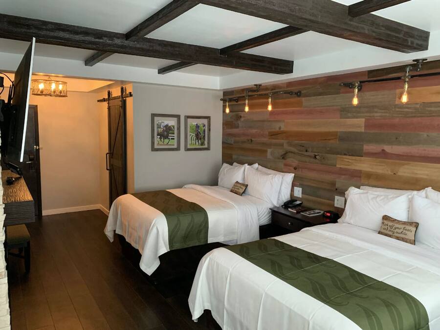 A hotel room with two beds, wooden headboard, and a staircase with a TV.