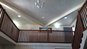 Un intérieur à plusieurs niveaux, agrémenté d’une rambarde en bois, d’un ventilateur de plafond, d’un éclairage encastré et d’œuvres d’art accrochées aux murs.