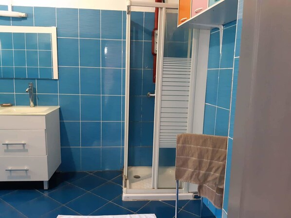 Une salle de bain avec des carreaux bleus, un lavabo blanc, un miroir et un espace douche.