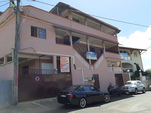 A two-story building with balconies, a sign for 'Cacao Lodge' and 'Chambre d'Hotel', and a parked car. - Cacao Lodge (Mamoudzou)