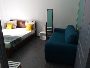 A bedroom with a bed, a blue sofa, a mirror, and a small white table. - Cacao Lodge (Mamoudzou)