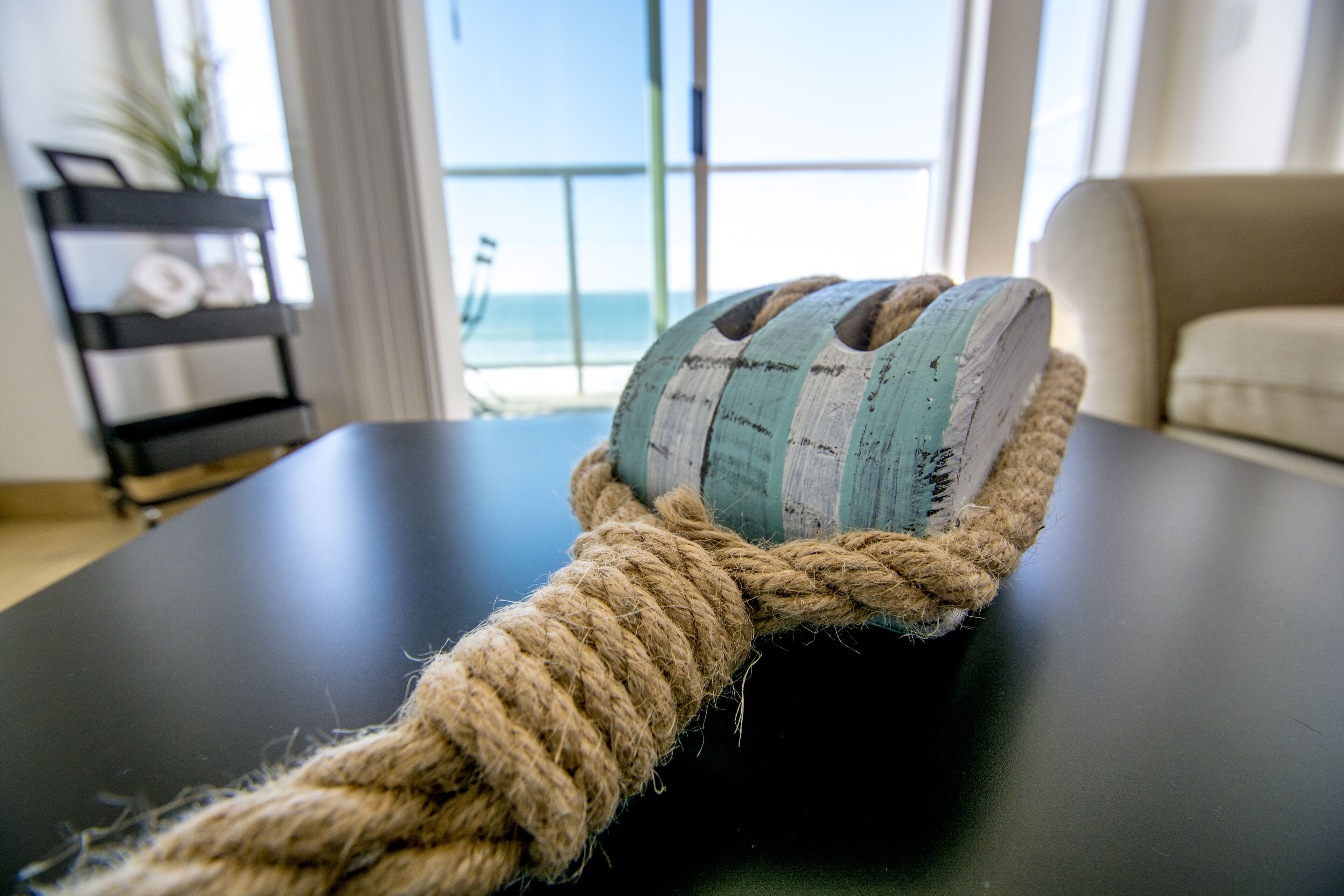 A rope tied around a black table in a room with a view of the ocean through large windows.