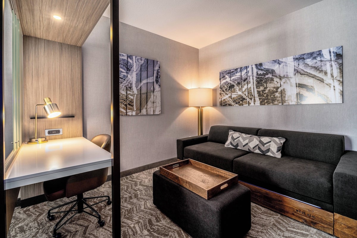 Une chambre d’hôtel moderne équipée d’un bureau, d’un canapé et de deux lampes fixées au mur.
