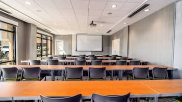 A conference room with a long table, multiple chairs, a projector screen, and a whiteboard.