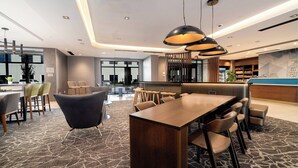 A modern hotel lobby with a wooden reception desk, comfortable seating, and a large window providing a view of the outside. - SpringHill Suites by Marriott Oakland Airport (Oakland)