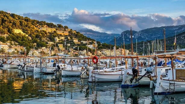 Una marina con imbarcazioni ormeggiate, circondata da edifici e colline.
