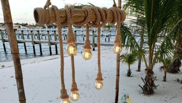 Un montaje para comer frente al mar, con mantel blanco, una pieza central bajo una cúpula de vidrio y una lámpara de cuerda.