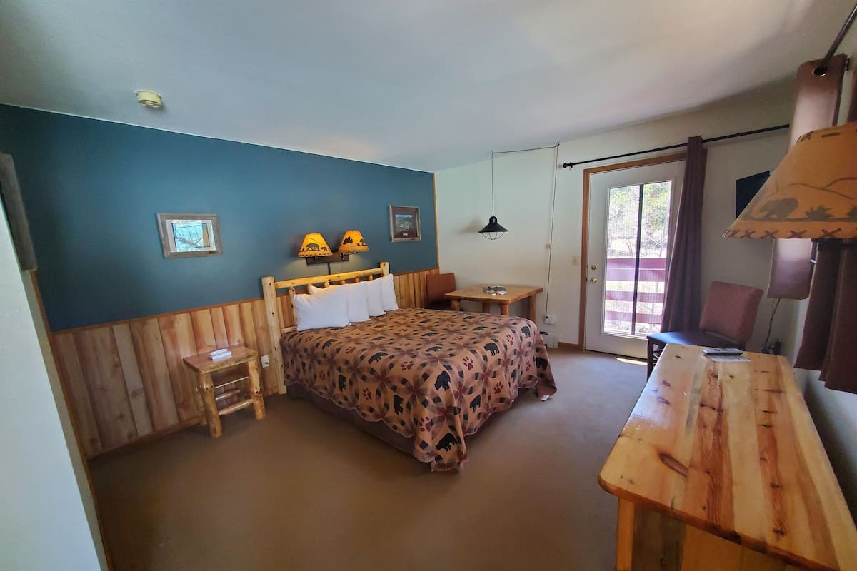 Ein Zimmer mit einem Bett, einem kleinen Tisch, einem Sessel und einem Schreibtisch. Zwei Wandleuchten und eine Deckenlampe sind vorhanden.