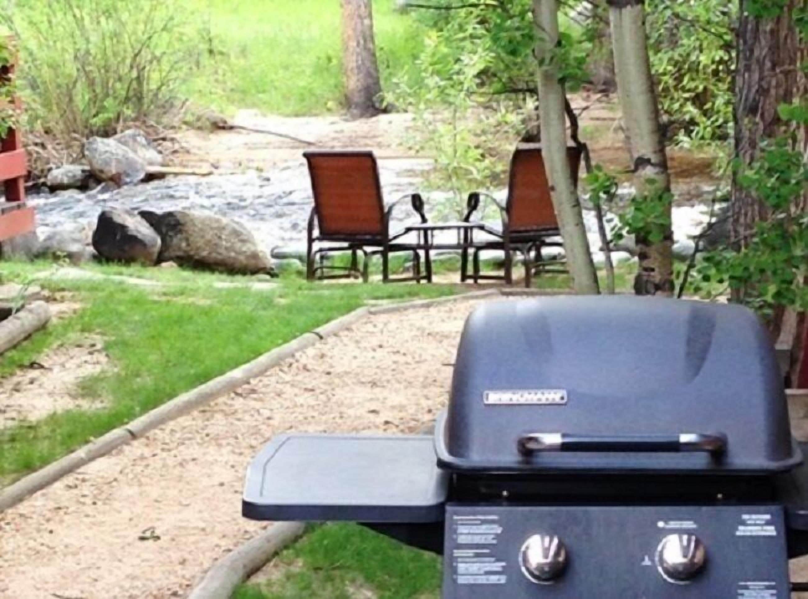 Una parrilla para barbacoa en un jardín con una mesa de picnic y sillas al fondo.